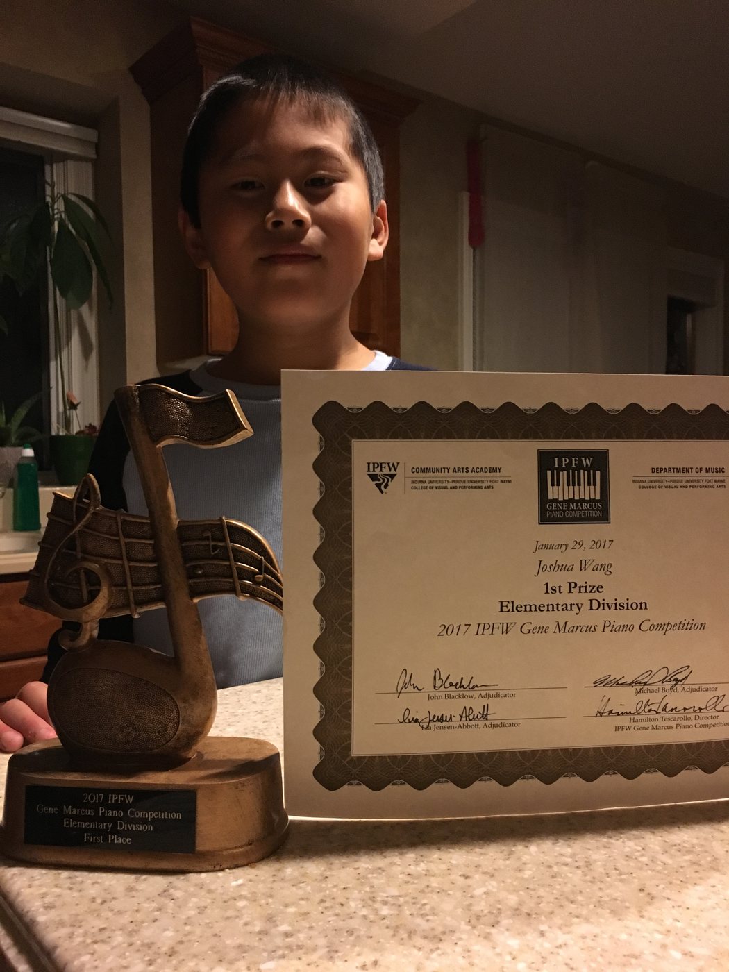 Joshua Wang holding a competition award certificate beside a trophy.