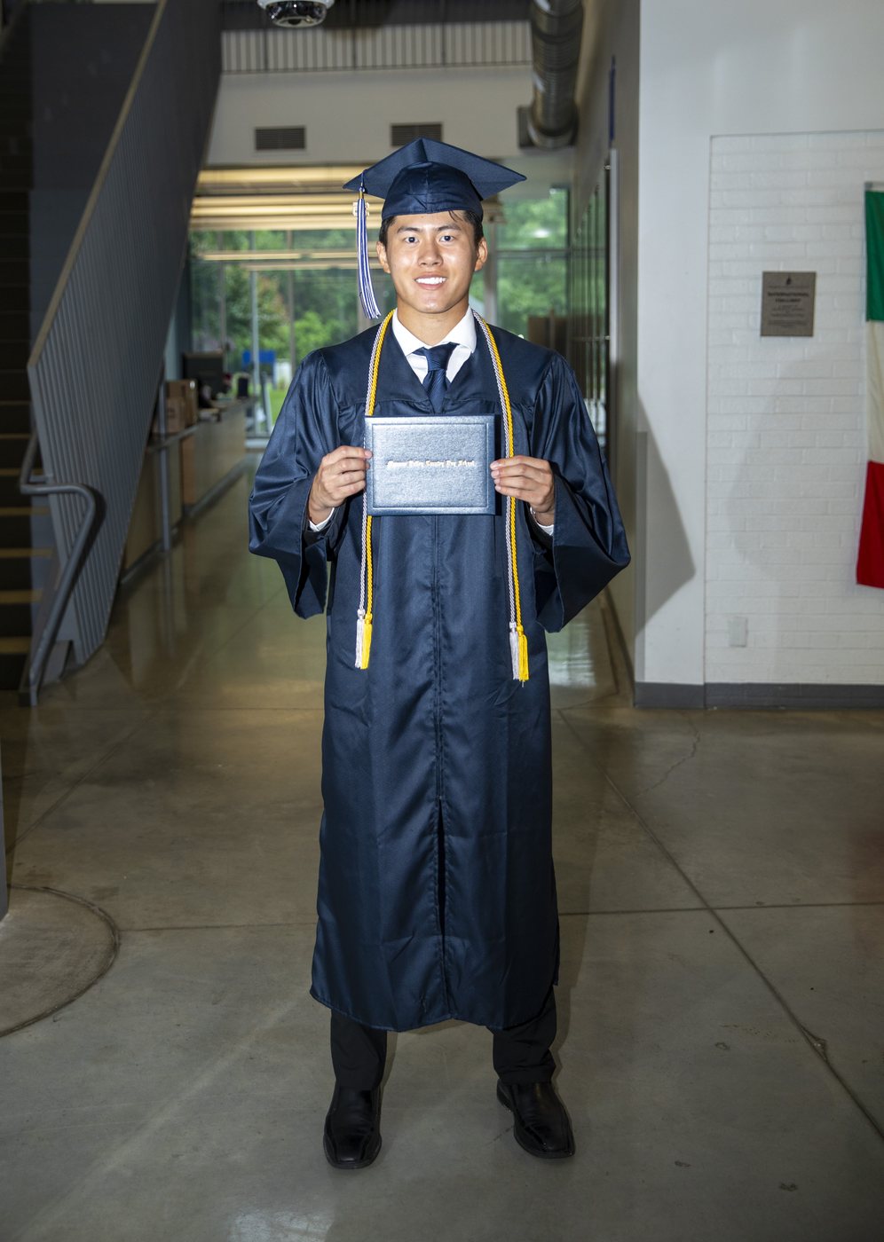Joshua Wang in graduation cap and gown holding his diploma.
