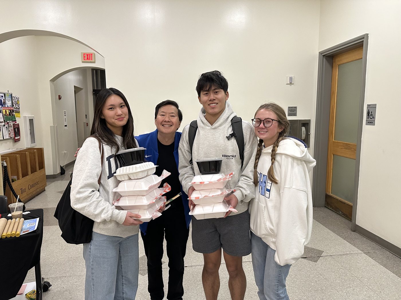 Joshua Wang and three friends indoors holding stacked takeout containers.