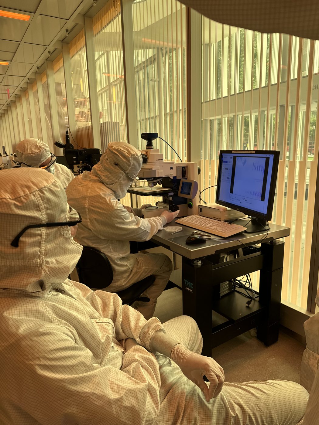 A researcher in full cleanroom coveralls working at a microscope station.
