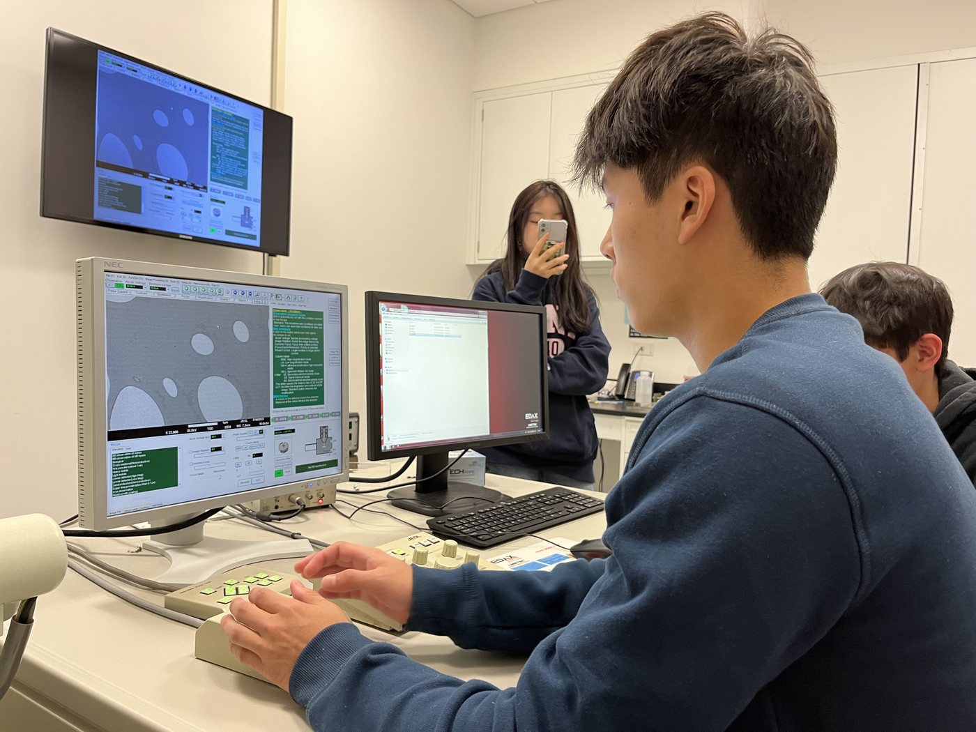Joshua Wang at a lab workstation with instrument software displayed on two monitors.