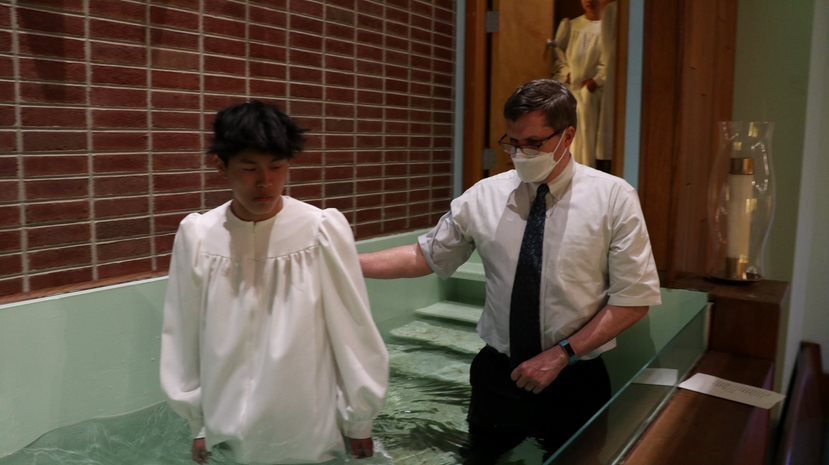 Joshua Wang stepping out of a baptismal pool alongside a church minister.