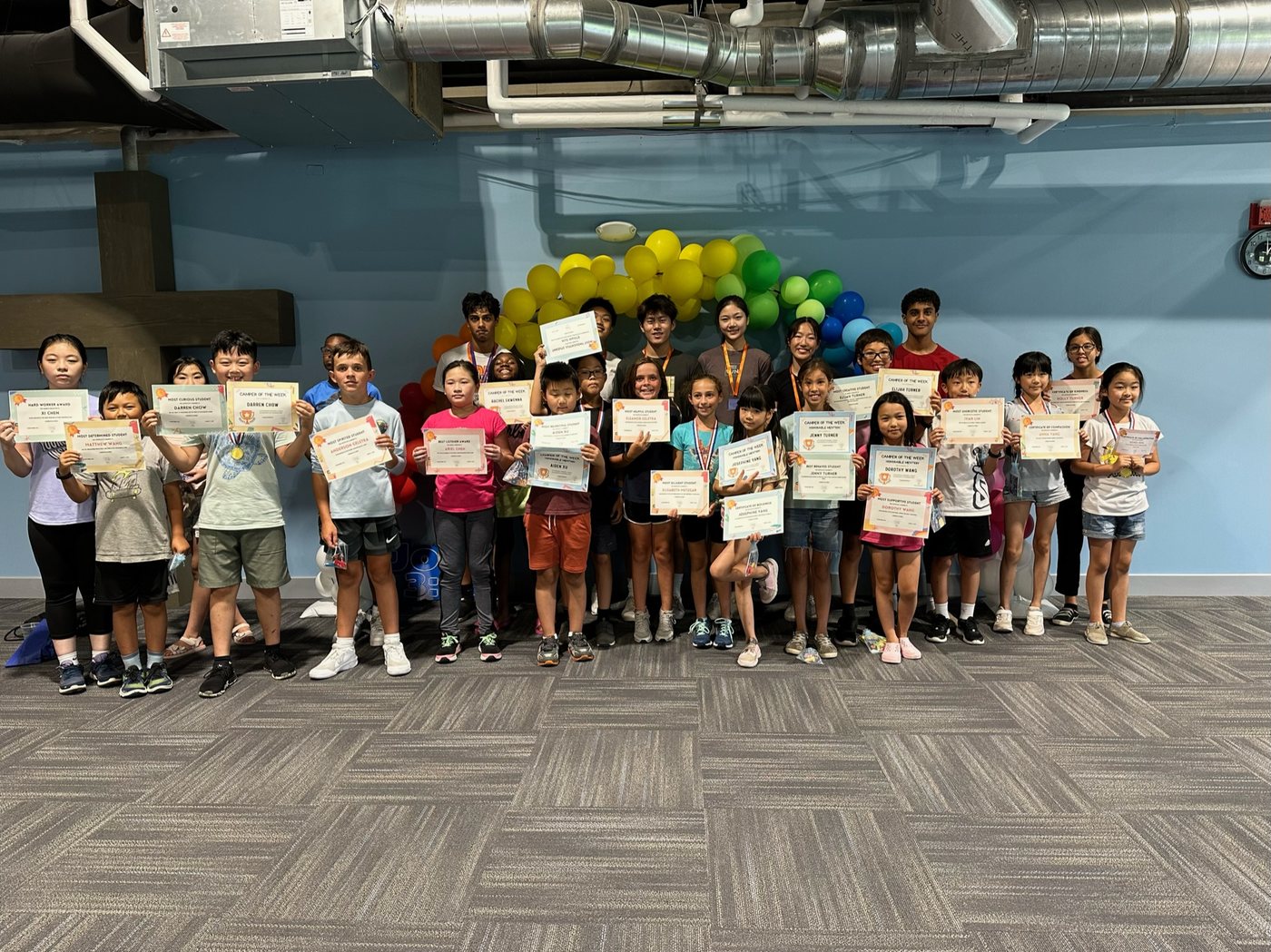 A large group of camp children holding certificates in front of balloon decorations.