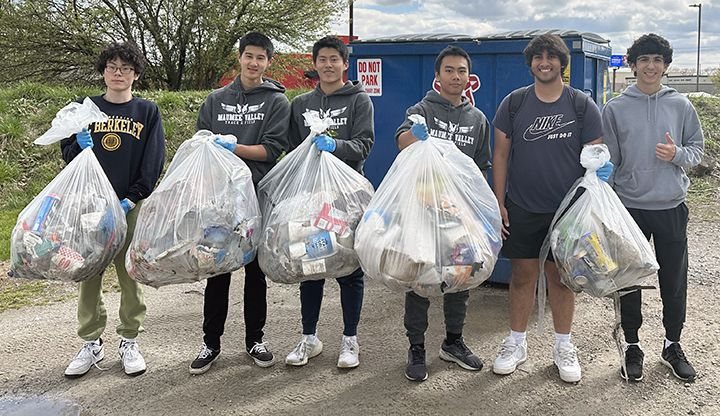 Volunteers standing outdoors holding filled bags of collected litter.